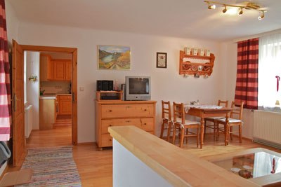 Gem&uuml;tliches Wohnzimmer mit Holzm&ouml;beln, Esstisch, Fernseher und roten Vorh&auml;ngen.