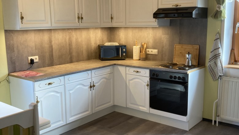 Ger&auml;umige K&uuml;che mit wei&szlig;en Schr&auml;nken, Herd, Mikrowelle und Holzdecke.