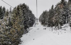 Sanfte Schneehügel erstrecken sich unter einem grauen Himmel, während der Sessellift gemächlich die Gäste in die Höhe befördert. Die winterliche Landschaft ist von einer ruhigen Stille umgeben, nur das Knirschen des Schnees unter den Skiern ist zu hören. Familien genießen die gemeinsame Zeit im Schnee und die Vorfreude auf rasante Abfahrten.
