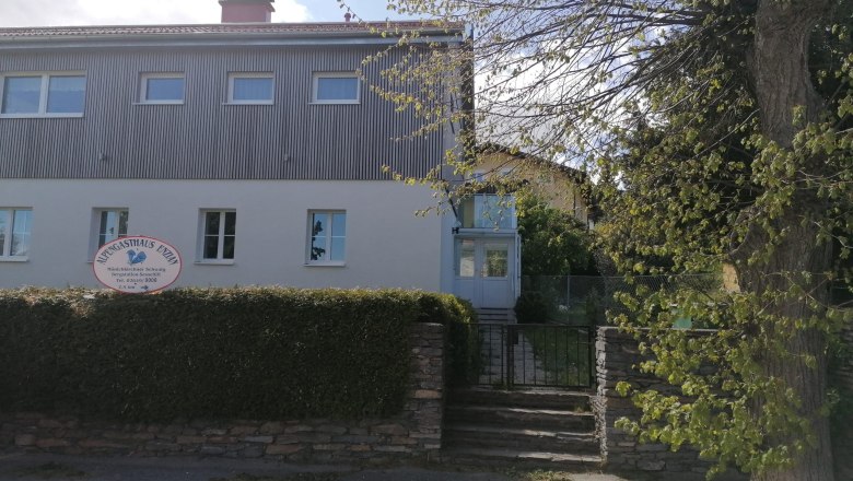 Zweist&ouml;ckiges Geb&auml;ude mit Schild 'Alpengasthaus Ewin' und Garten.