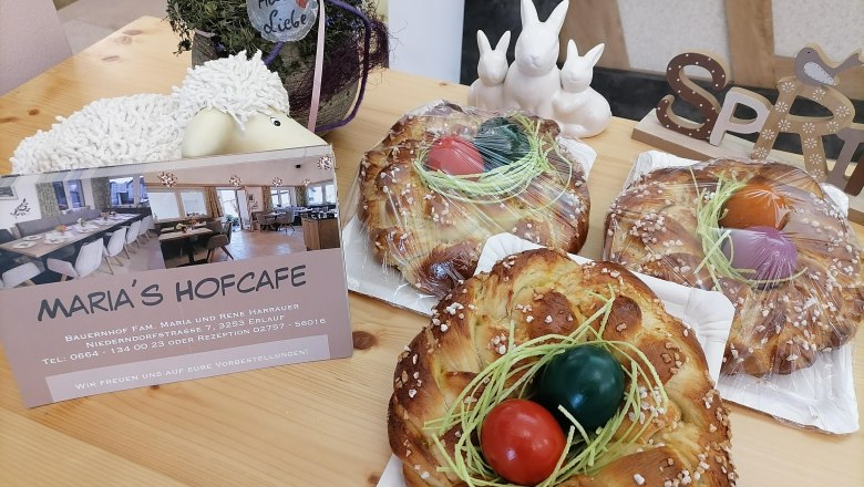 Drei Osterkr&auml;nze mit bunten Eiern auf einem Tisch, daneben eine Karte von Maria's Hofcafe und Osterdekoration.