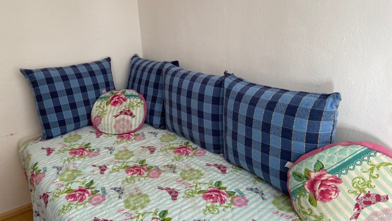 Ein Kinderzimmer mit einem Ausziehbett, das mit einer gebl&uuml;mten Decke und blauen Kissen dekoriert ist.