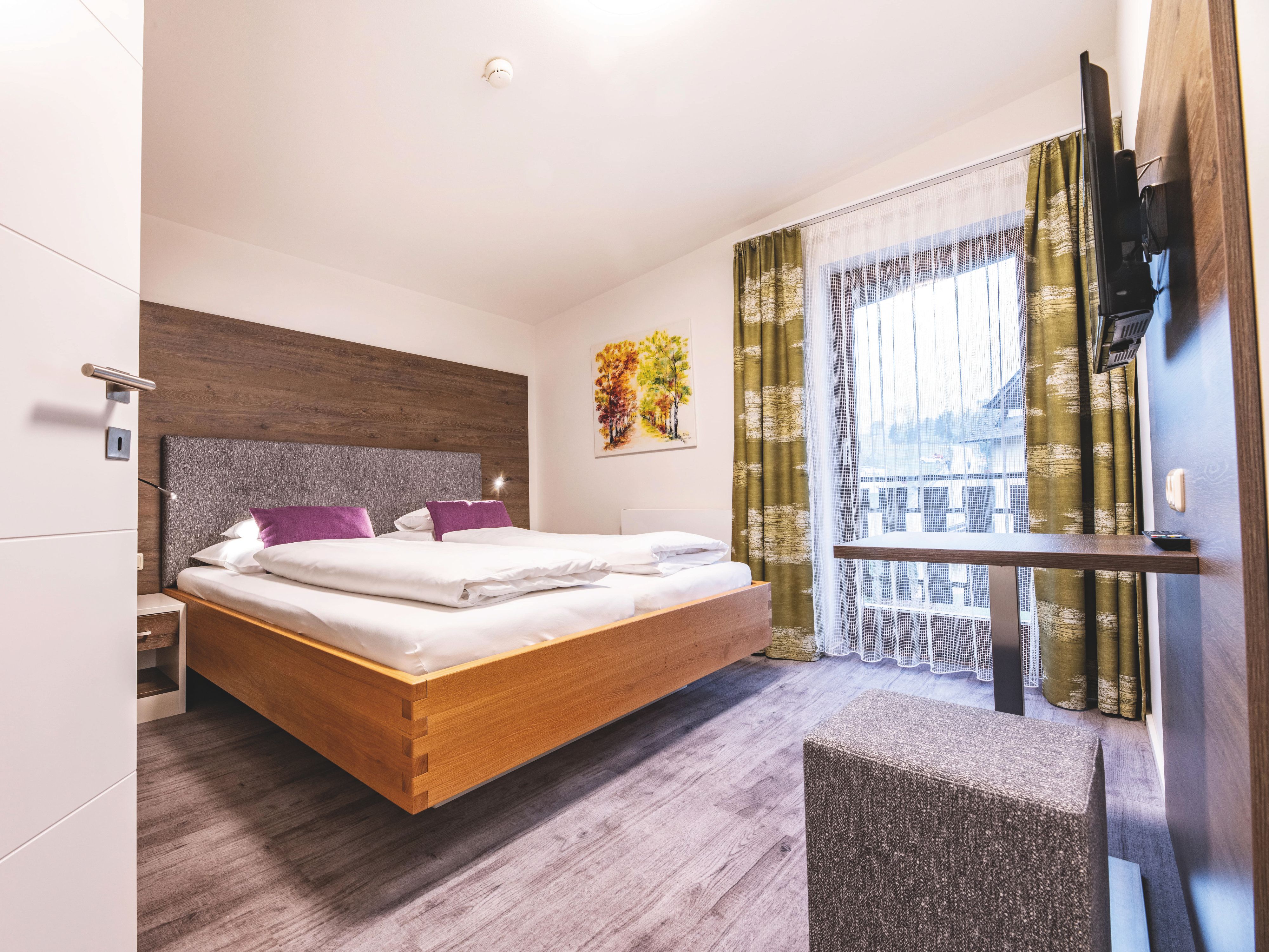 Modern eingerichtetes Hotelzimmer mit Doppelbett, Kissen, Holzmöbeln und Balkon.