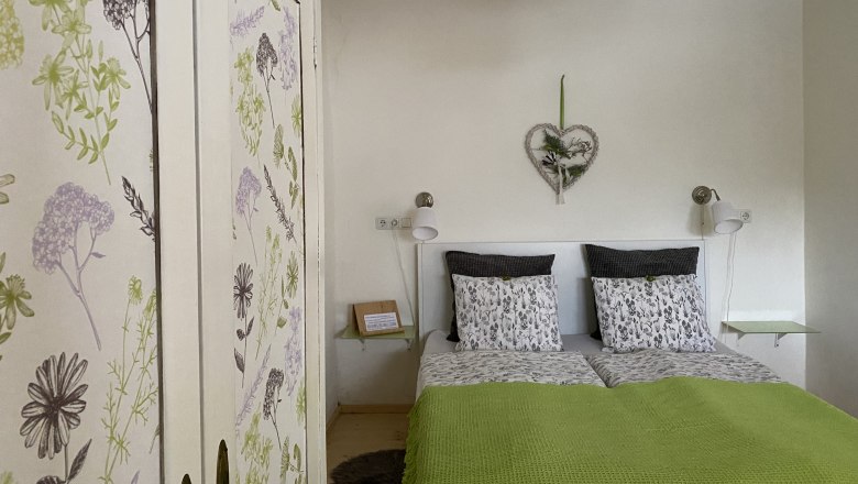 Gem&uuml;tliches Doppelzimmer mit floralem Kleiderschrank und gr&uuml;ner Bettdecke.