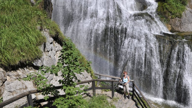 Eine Frau steht auf einer Treppe vor einem Wasserfall in der Wasserlochklamm Palfau.