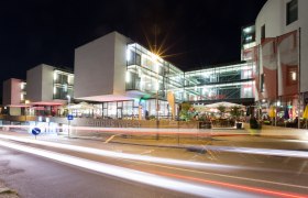 Nachtaufnahme eines modernen Gebäudekomplexes mit Glasfassade und beleuchteten Innenräumen.