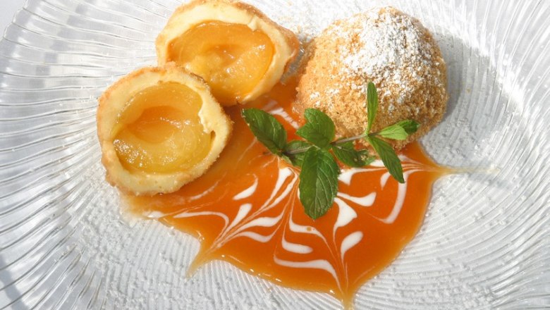 Wachauer Marillenkn&ouml;del auf einem Teller mit Aprikosensauce und Minzbl&auml;ttern dekoriert.