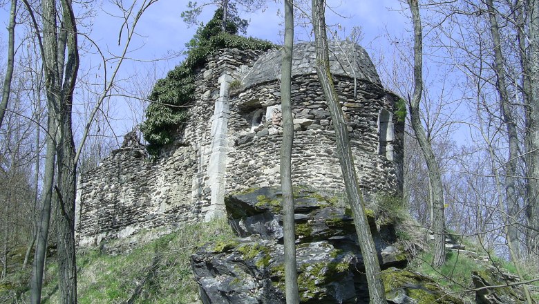 Ruine in einem Wald mit Bäumen und blauem Himmel.