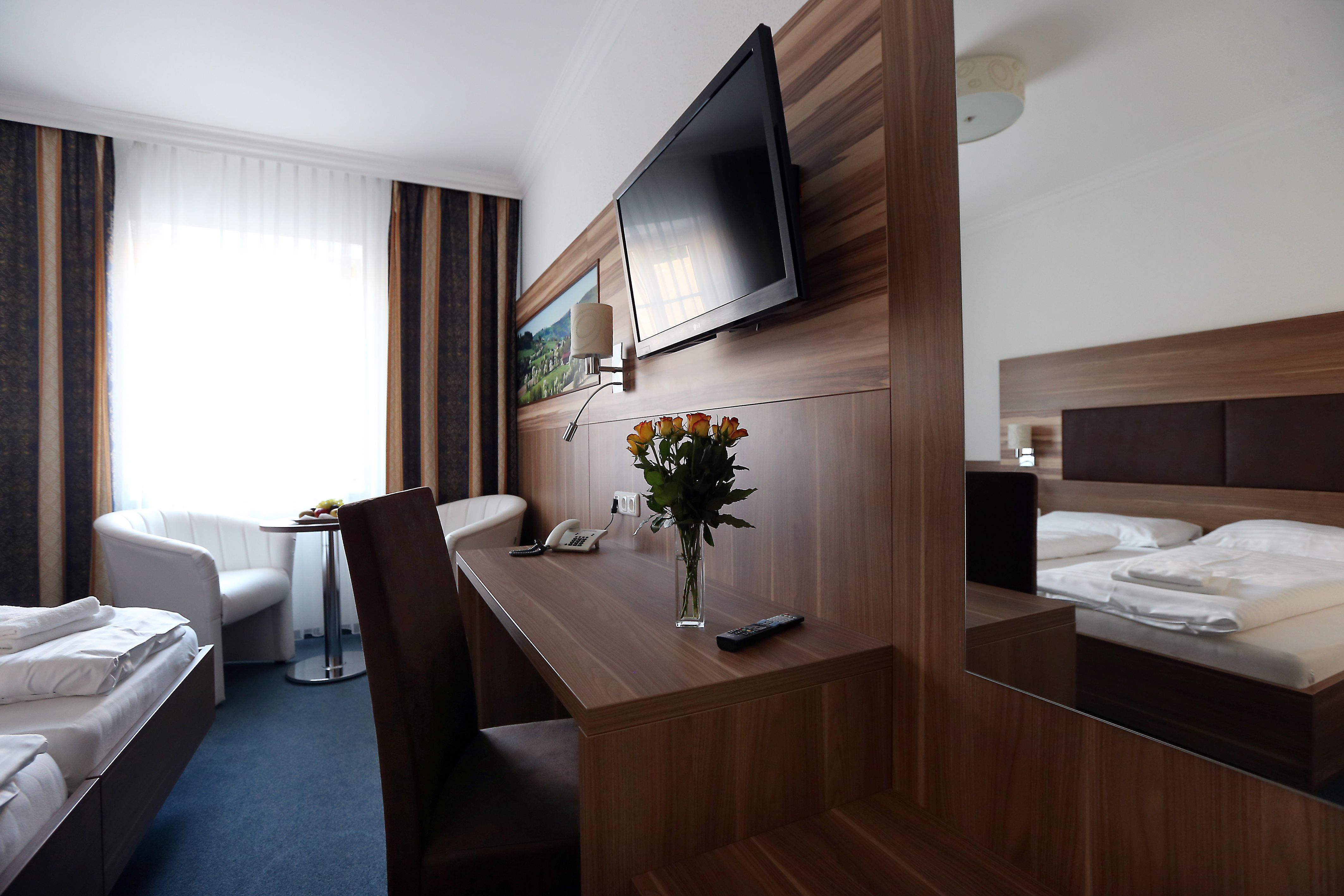Modern eingerichtetes Hotelzimmer mit Doppelbett, Schreibtisch, Flachbildfernseher und Blumenstrauß.