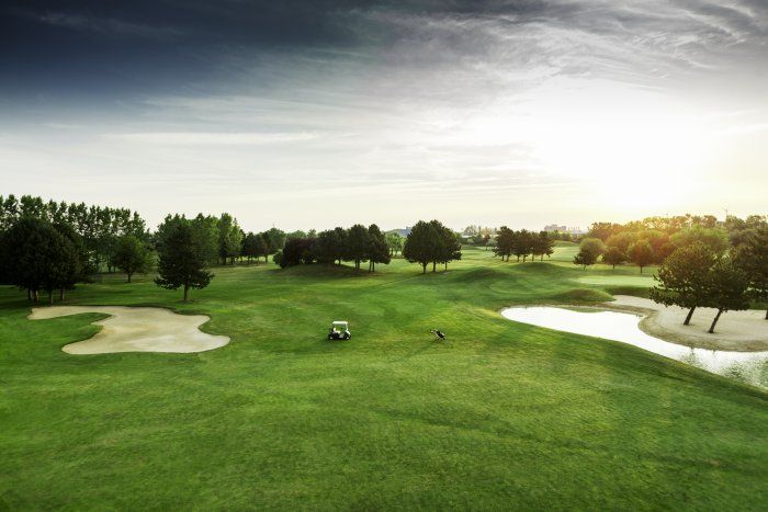 Golfplatz mit grünen Fairways, Sandbunkern und einem Golfwagen bei Sonnenuntergang.