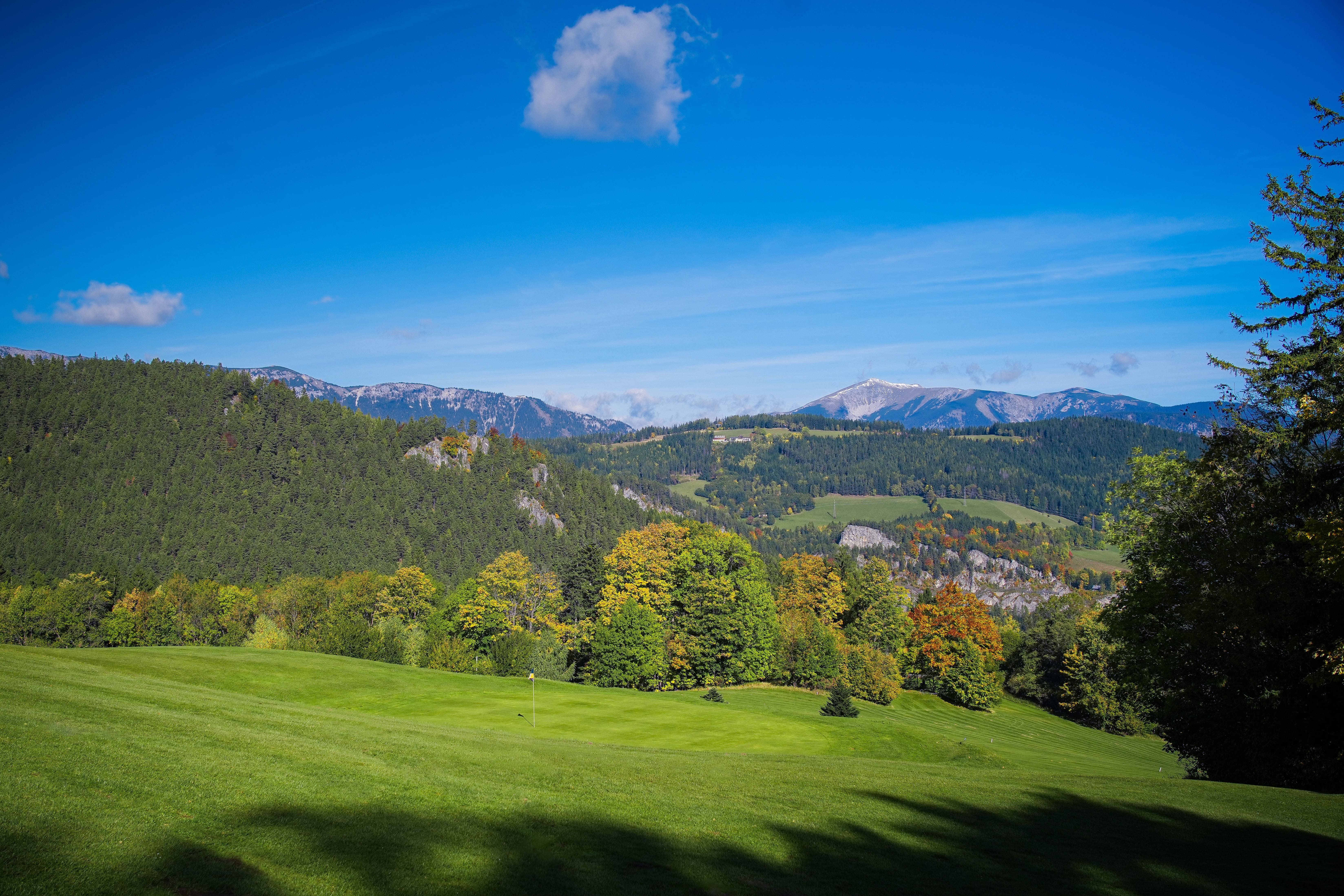 Blick auf eine grüne Landschaft mit Hügeln und Bergen im Hintergrund, unter einem klaren blauen Himmel.