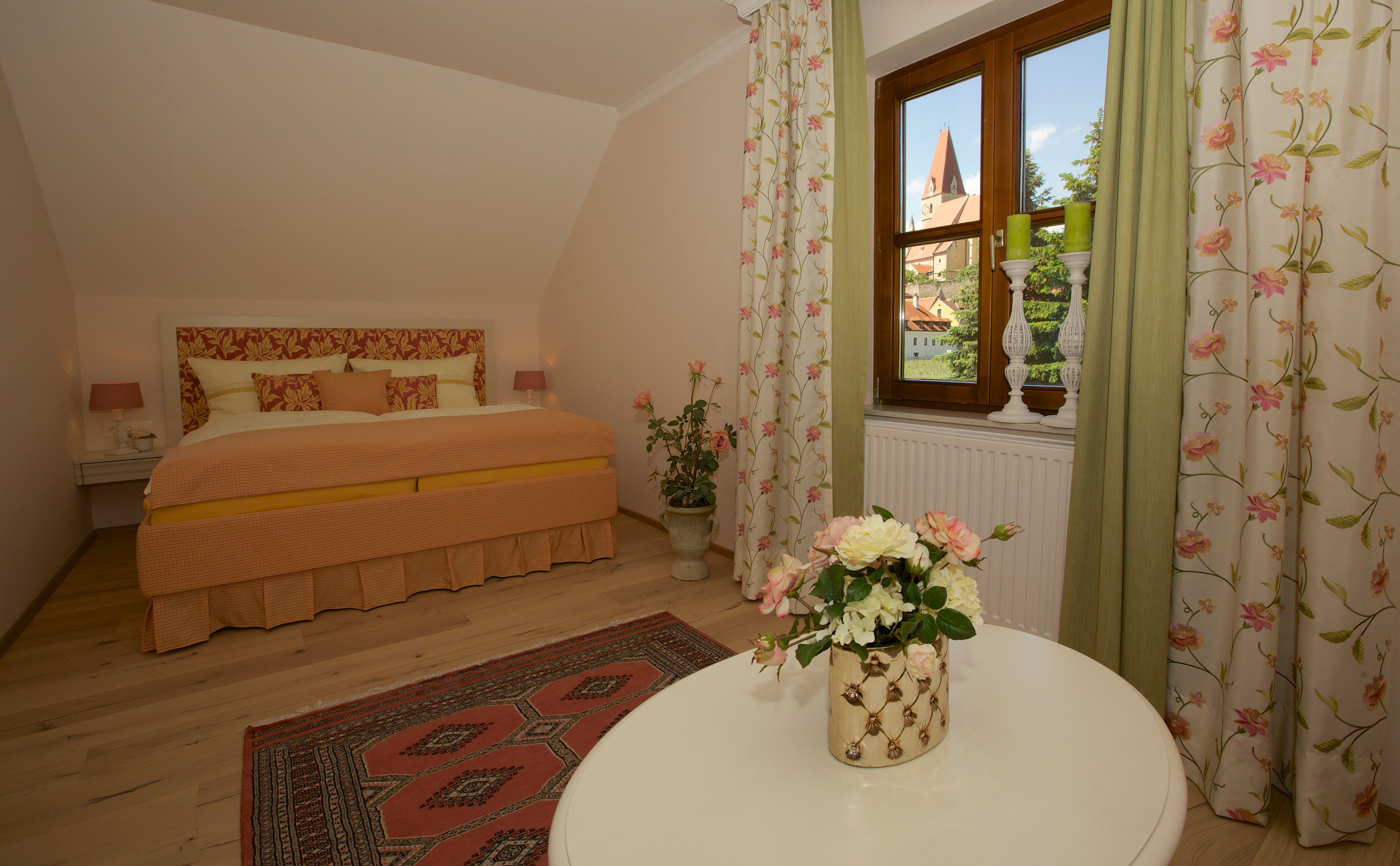 Gemütliches Schlafzimmer mit Blumenmuster und Blick auf eine Kirche durch das Fenster.