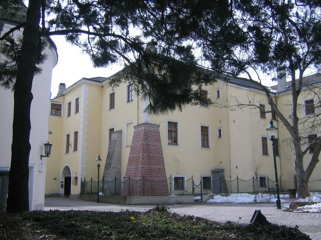 Schloss Purkersdorf im Winter mit schneebedecktem Boden und Bäumen im Vordergrund.