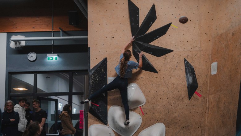 Eine Frau klettert an einer Indoor-Kletterwand mit schwarzen und weißen Griffen.