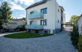 Modernes dreistöckiges Gebäude mit Balkonen und gepflastertem Hof.