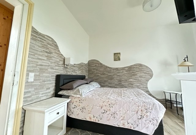 Ein gem&uuml;tliches Schlafzimmer mit einem Einzelbett, floralem Bettbezug, Nachttisch und dekorativer Wandgestaltung.