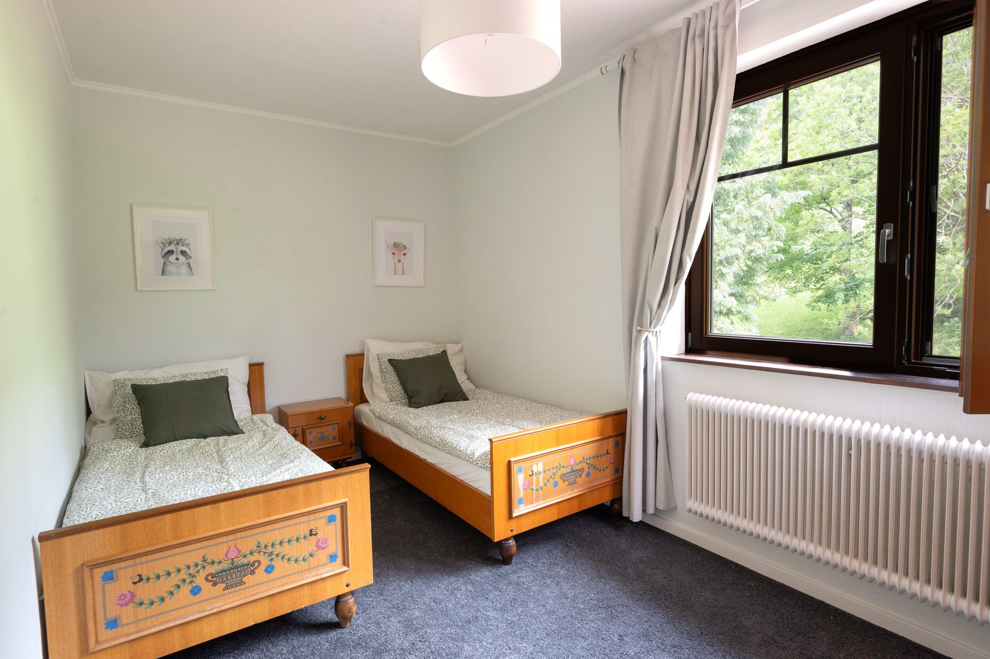 Schlafzimmer mit zwei Einzelbetten, Holzmöbeln und einem großen Fenster mit Blick ins Grüne.