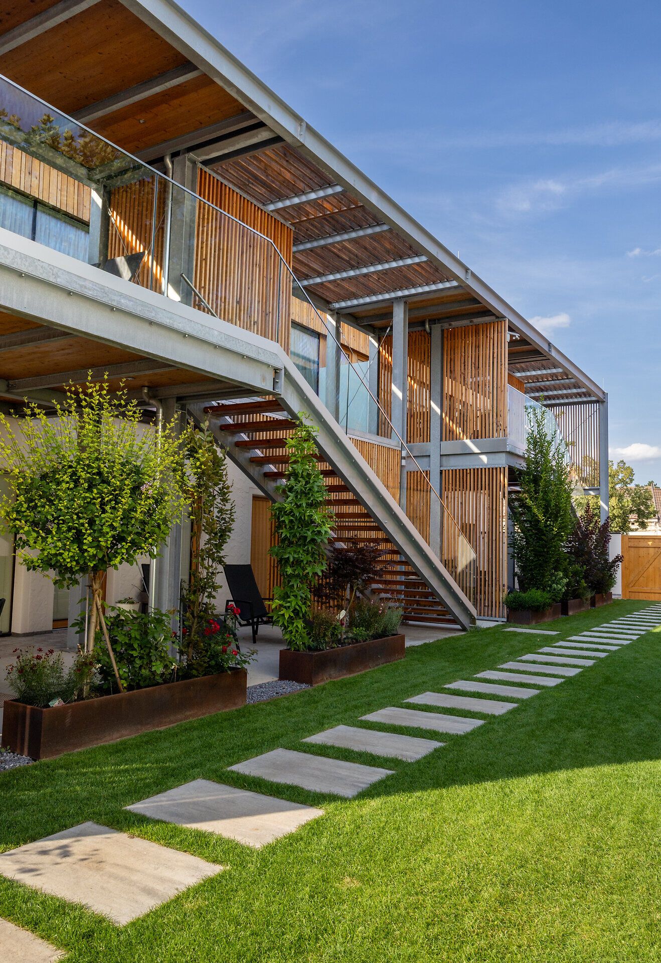 Modernes Gebäude mit weißer Fassade und Holzelementen, umgeben von einer Mauer mit Holztor.