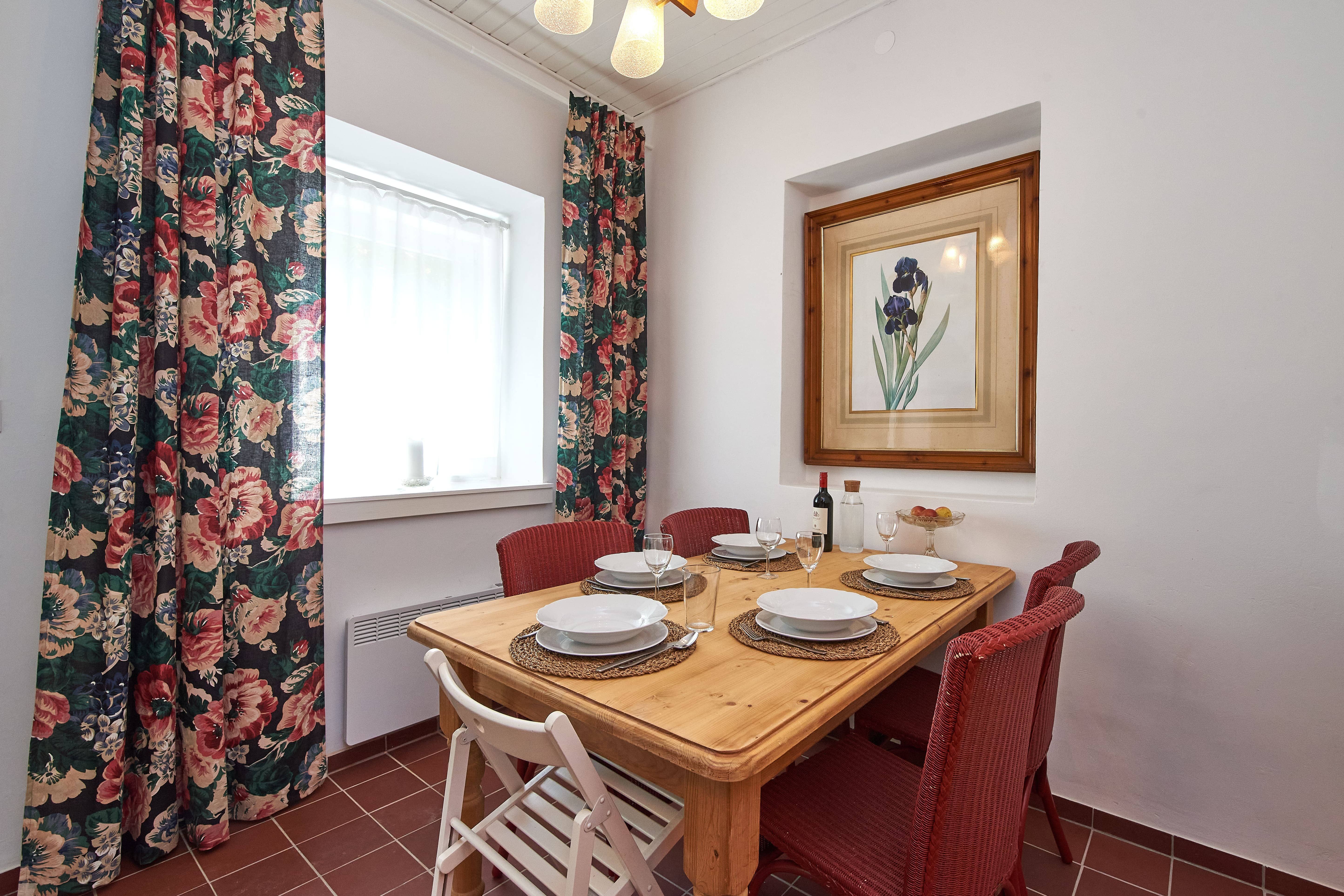 Ein Esstisch mit vier Gedecken, roten Stühlen und einem Blumenbild an der Wand.