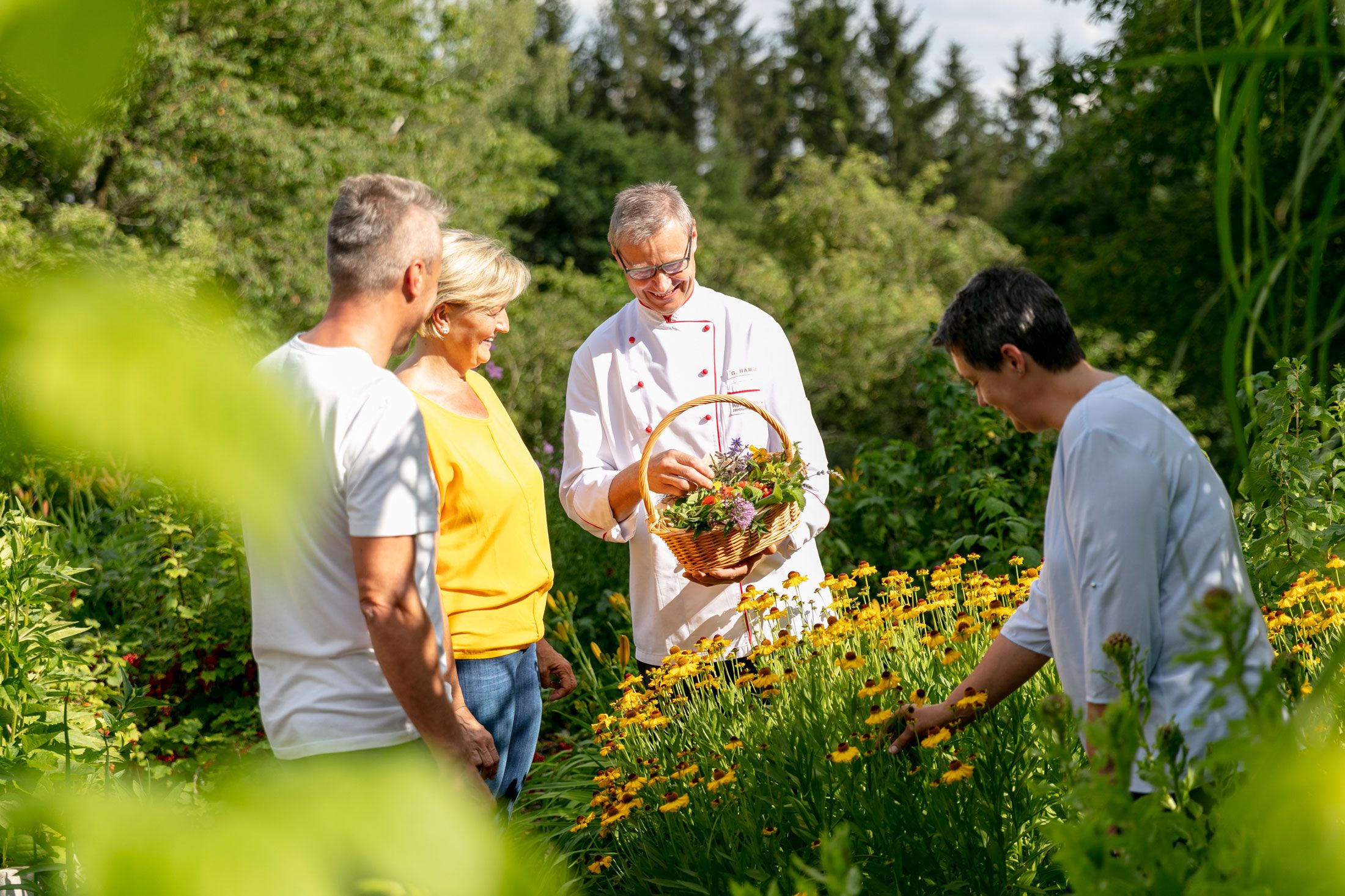 Vier Personen in einem Kräutergarten, eine Person hält einen Korb mit Kräutern.