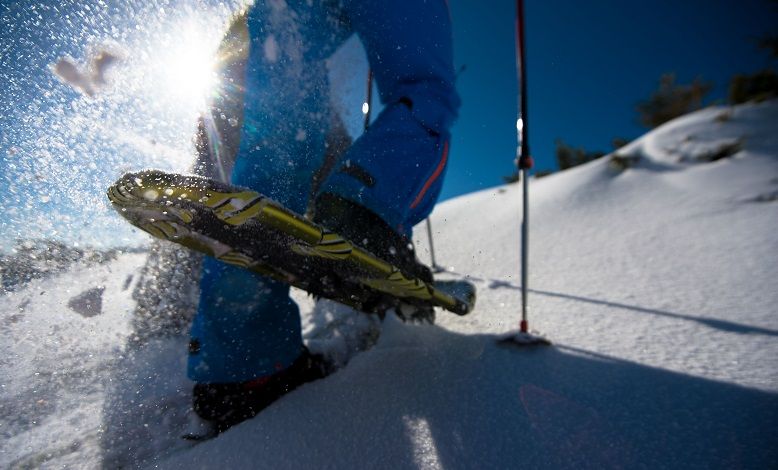 Nahaufnahme eines Schneeschuhs im Schnee mit Sonnenlicht im Hintergrund.