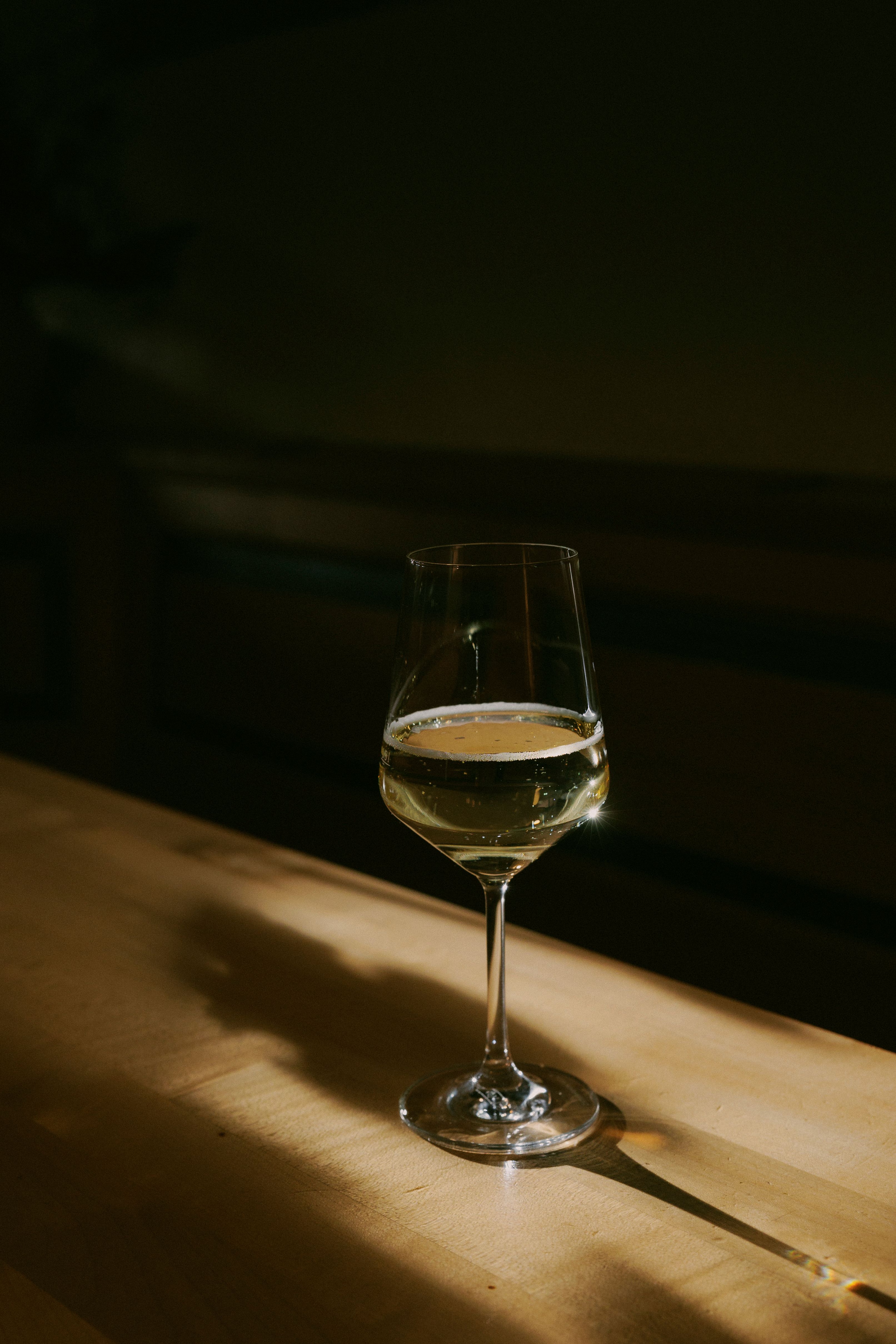 Ein Weinglas mit Weißwein steht auf einem Holztisch, beleuchtet von einem warmen Lichtstrahl.