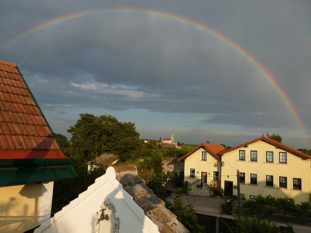 Ein Regenbogen über einem Dorf mit gelben Häusern und roten Dächern.