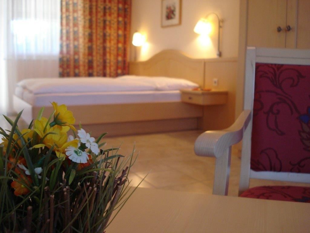 Ein gemütliches Gästezimmer mit einem Bett, einem Stuhl und einem Tisch mit Blumen.