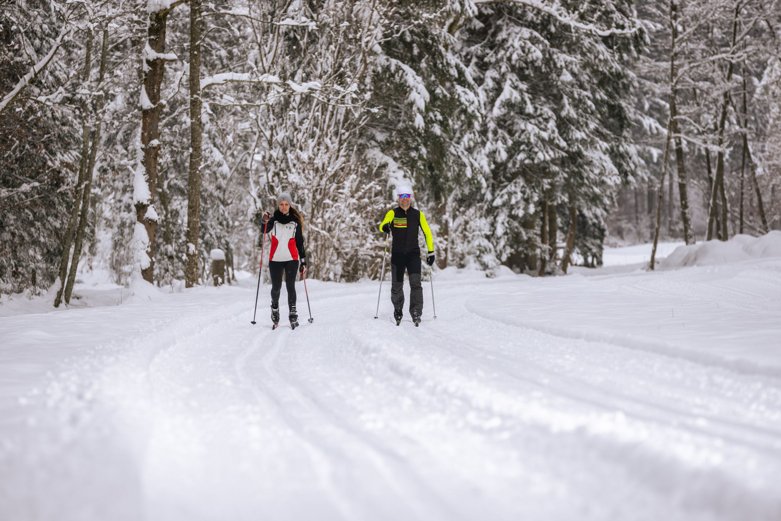Zwei Personen beim Skilanglauf auf einer verschneiten Waldloipe.