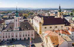 Der Rathausplatz in St. Pölten strahlt eine einladende Atmosphäre aus, umgeben von historischen Gebäuden und lebhaften Straßen. Die sanften Hügel im Hintergrund bieten einen malerischen Kontrast zur urbanen Szenerie und laden dazu ein, die Schönheit der Stadt zu erkunden.