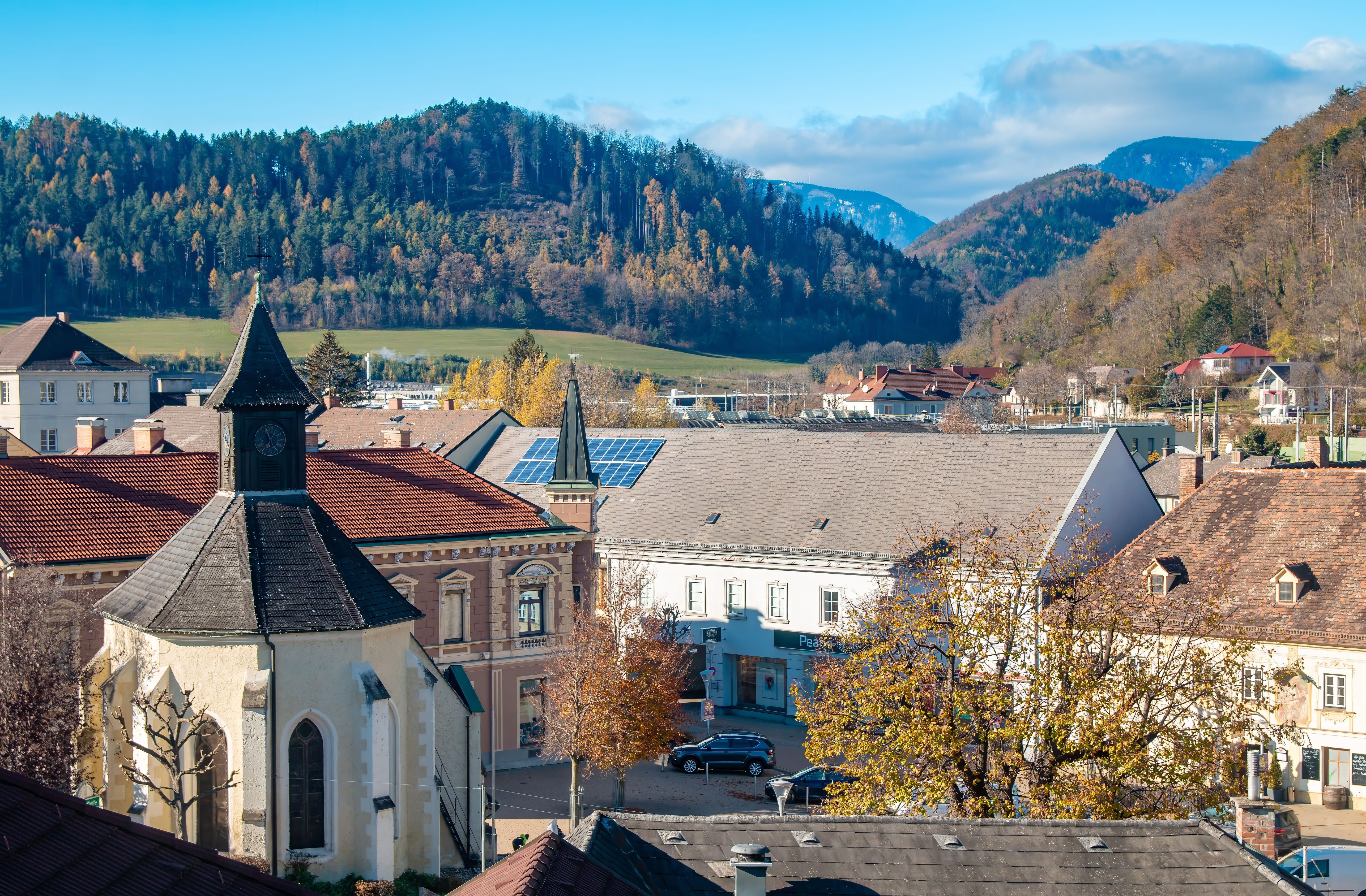 Stadtansicht von Gloggnitz mit Kapelle, Gebäuden und bewaldeten Hügeln im Hintergrund.