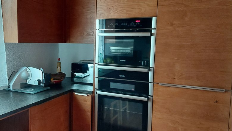 Moderne K&uuml;che mit Holzschr&auml;nken, eingebautem Ofen und Arbeitsplatte mit K&uuml;chenger&auml;ten.