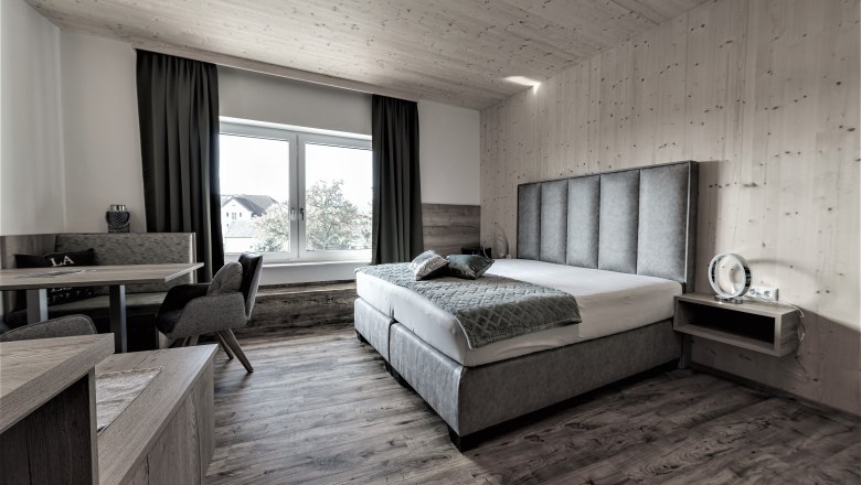 Modern eingerichtetes Hotelzimmer mit Doppelbett, Sitzbereich und gro&szlig;em Fenster.
