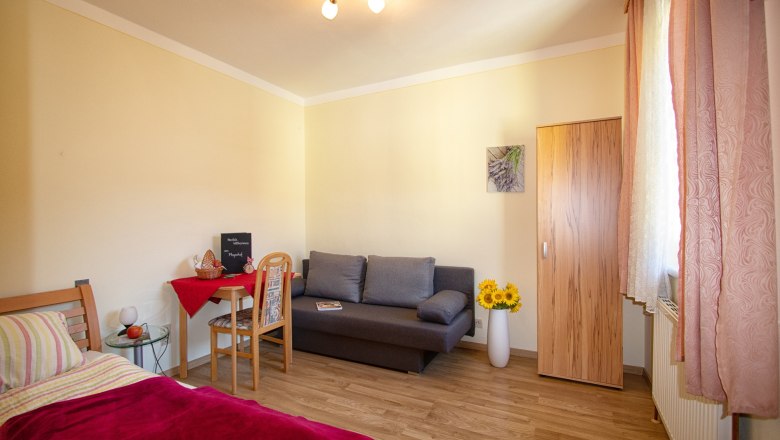 Gem&uuml;tliches Zimmer mit Bett, Sofa, Tisch und Schrank, dekoriert mit Sonnenblumen und einem Bild an der Wand.