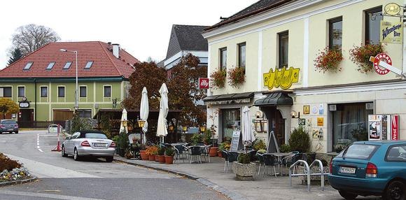 Gasthof Mostlandl Aussenansicht, © Leopold Rank Außenansicht von einem Gasthaus an einem Belebten Platz mit Bäumen, Sonnenschirmen, Sesseln uvm.