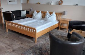 Gem&uuml;tliches G&auml;stezimmer mit Doppelbett, Ledersesseln und dekorativem Bild an der Wand.