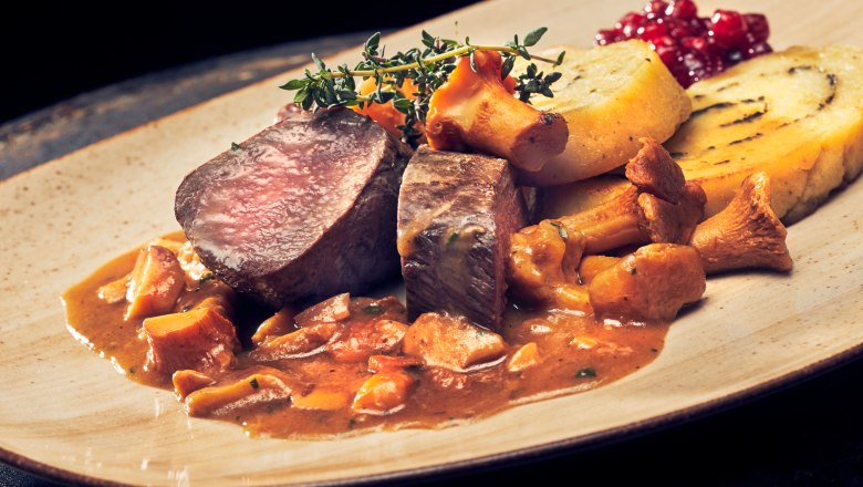 Rehr&uuml;cken mit Eierschwammerlsauce und Erd&auml;pfel-Kr&auml;uterroulade auf einem Teller.