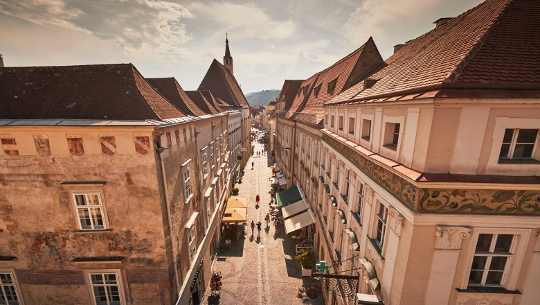 Blick auf eine historische Stra&szlig;e in der Altstadt von Krems mit alten Geb&auml;uden und Menschen, die spazieren gehen.