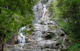 Ein Wasserfall flie&szlig;t &uuml;ber Felsen in einem bewaldeten Gebiet.