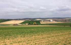 Landschaft mit Feldern und Bauernhof in der Ferne.