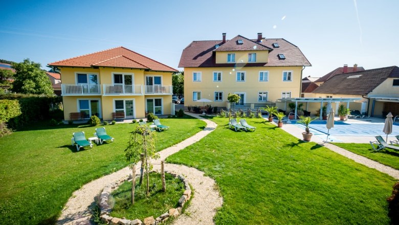 Gartenanlage mit gelben Geb&auml;uden und Liegest&uuml;hlen bei sonnigem Wetter.
