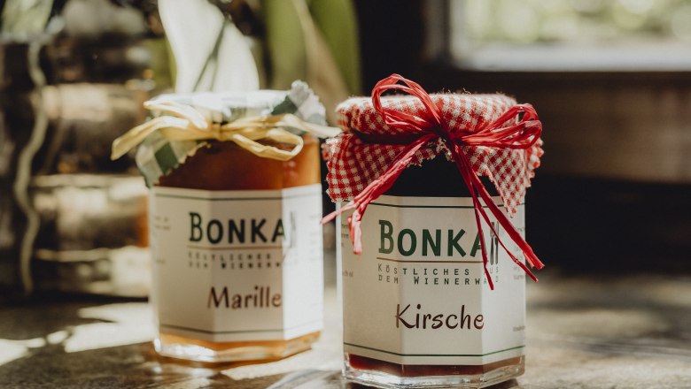 Zwei Gl&auml;ser Marmelade mit Etiketten 'Bonka', eins mit Marille, das andere mit Kirsche, auf einem Tisch.