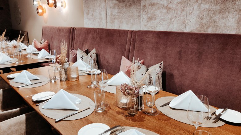 Ein elegant gedeckter Tisch in einem Restaurant mit weißen Servietten, Gläsern und Besteck auf Holzoberfläche.