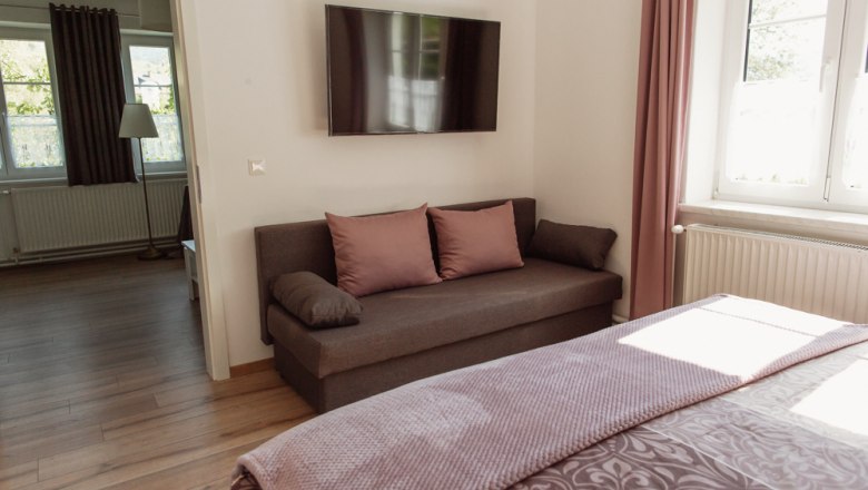 Modernes Wohnzimmer mit Sofa, Flachbildfernseher und Fenster mit rosa Vorhängen.