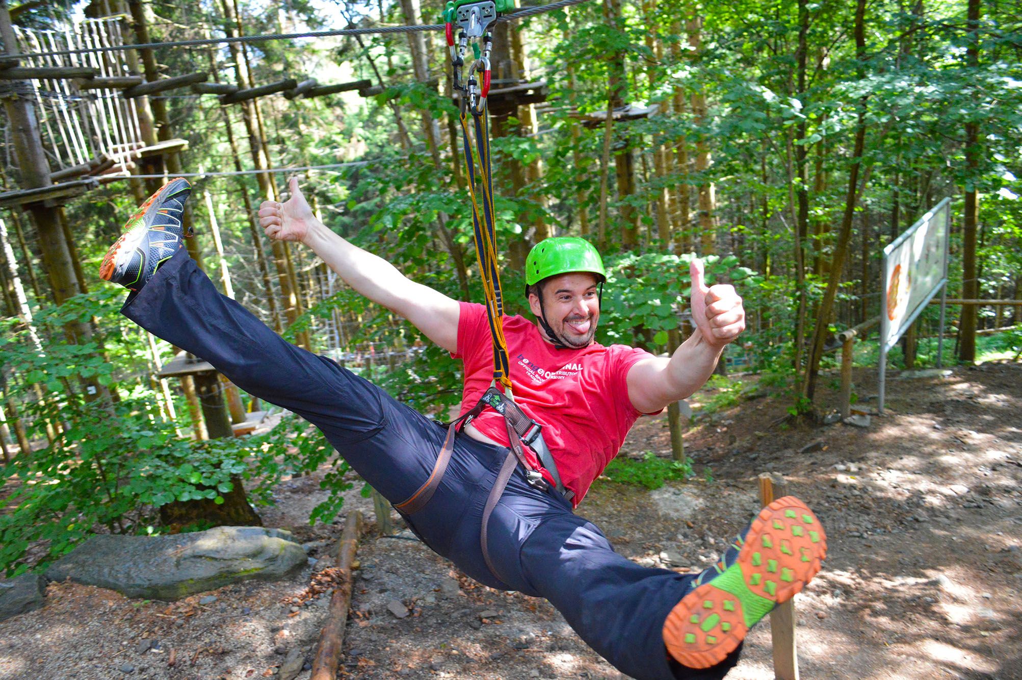 Person mit Helm und Sicherheitsgurt auf einer Seilrutsche im Wald.