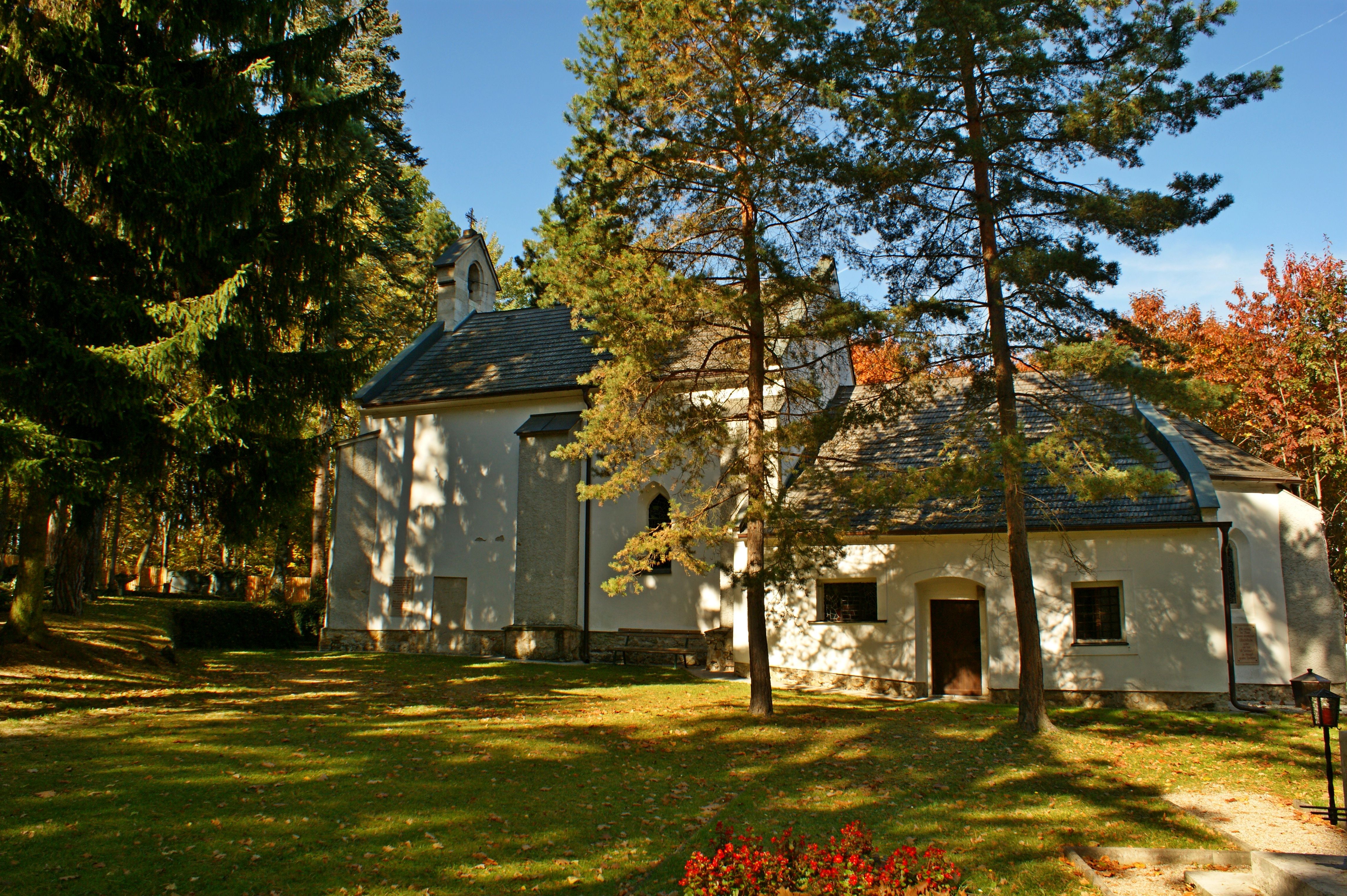 Eine kleine Kirche im Wald, umgeben von Bäumen und herbstlichem Laub.