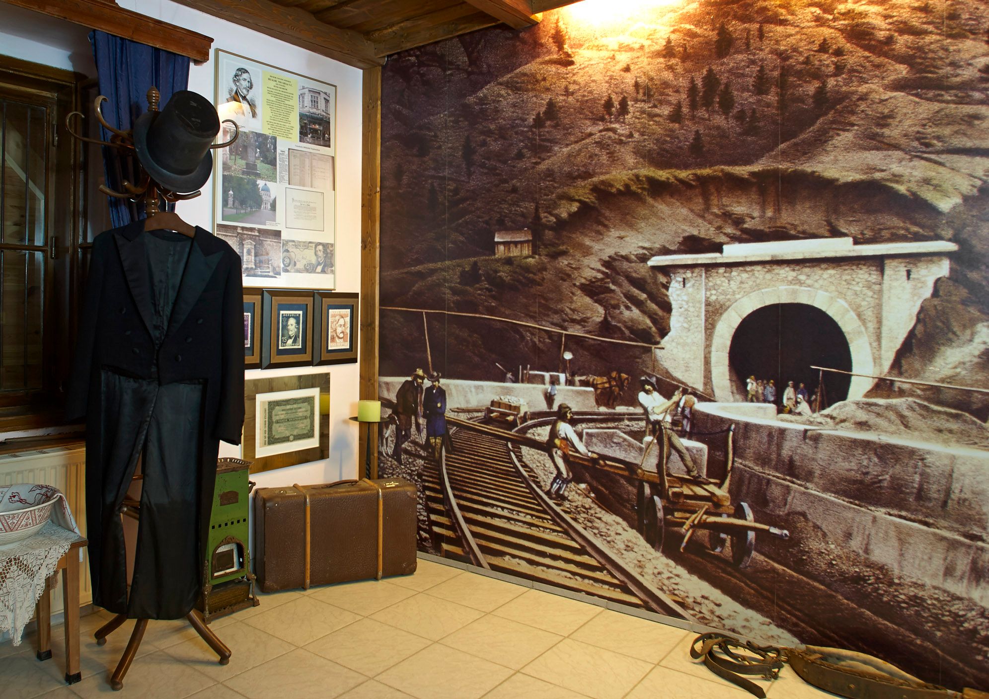 Innenansicht des Ghega Museums mit historischem Anzug, Bildern und einer großen Wandmalerei eines Eisenbahntunnels.