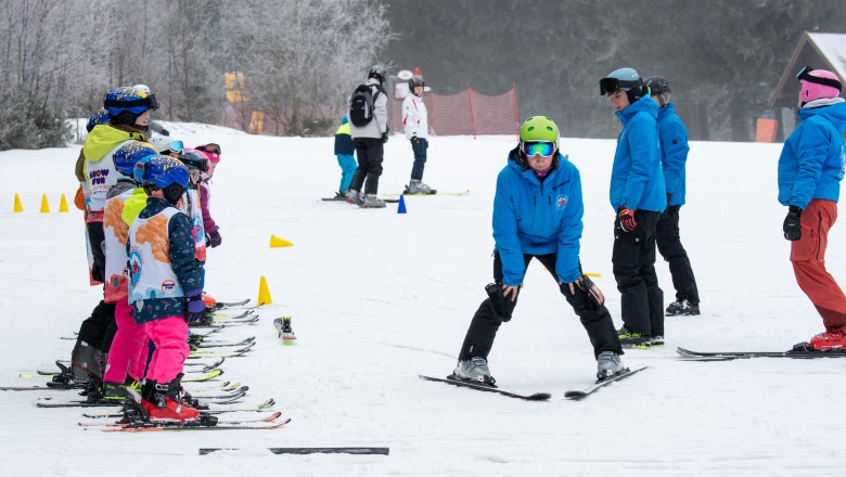 Skilehrer zeigt Kindern auf Skiern eine Übung auf einer Skipiste.
