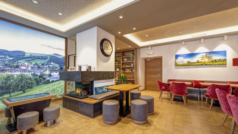 Innenansicht eines modernen Bistros mit Kamin, roten St&uuml;hlen und gro&szlig;em Landschaftsbild an der Wand.