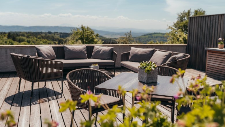 Terrasse mit Sitzm&ouml;beln und Pflanzen, im Hintergrund eine weite Landschaft.